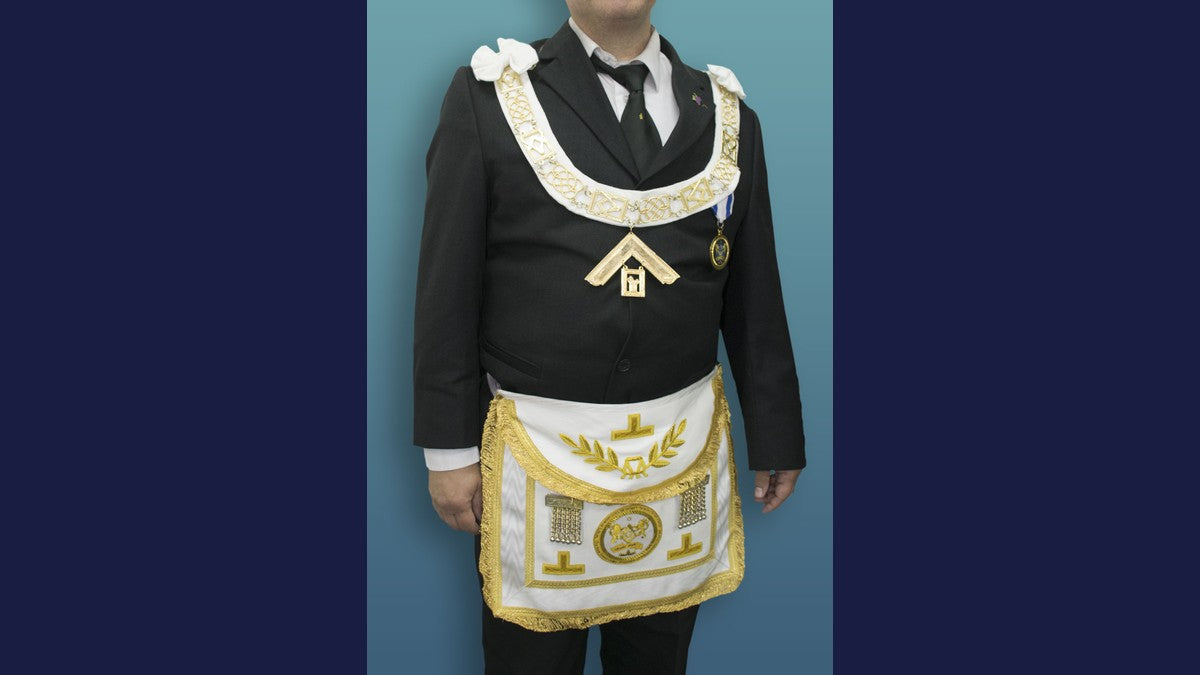 Freemason wearing a white-and-gold ceremonial apron, collar and jewel over a dark suit