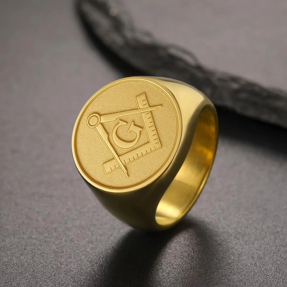 Gold-tone engraved Masonic ring beside dark rock