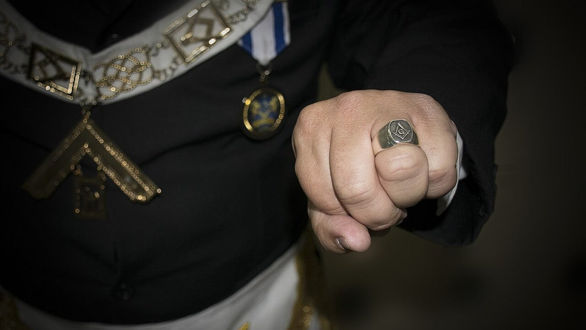 Masonic ring worn on a hand beside ceremonial regalia